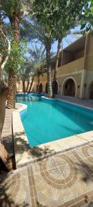 a swimming pool with palm trees and a building at Nour El Waha Hotel in Siwa
