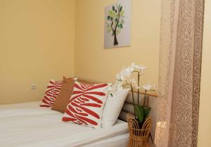 Momento Apartment في كيوستينديل: سرير مع وسائد حمراء وبيضاء و مزهرية مع الزهور