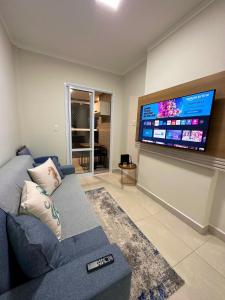 ein Wohnzimmer mit einem blauen Sofa und einem Flachbild-TV in der Unterkunft Canto do Forte, Próx. á Praia, Churrasqueira, Ar-cond, Wi-fi ,Vaga de Garagem, Acomoda até 5 pessoas in Praia Grande