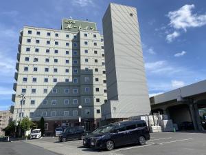 un grand bâtiment blanc avec des voitures garées dans un parking dans l'établissement Hotel Route-Inn Hon Hachinohe Ekimae, à Hachinohe