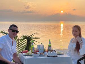 a man and woman sitting at a table in front of the ocean at Thoddoo Island Holiday Inn in Thoddoo