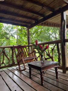 a wooden porch with two chairs and a vase with flowers at Refugio del Bosque CABAÑAS Y GLAMPING in Guácimo