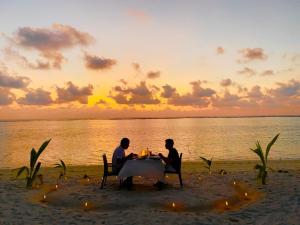 dos personas sentadas en una mesa en la playa al atardecer en Thoddoo Island Holiday Inn en Thoddoo