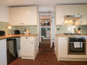 a kitchen with white cabinets and a brick floor at Tubs Cottage in Kingsteignton