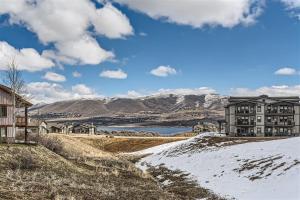 a building on a snowy hill with a lake and mountains at Helling Circle Hideaway 303 condo in Heber City