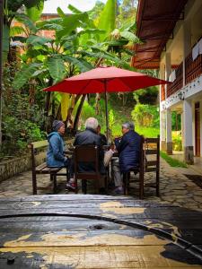 trzy osoby siedzące na ławkach pod czerwonym parasolem w obiekcie Killa Wasi B&B w mieście Chachapoyas