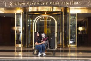 dos mujeres sentadas en un banco frente a un edificio en Sheraton Mexico City Maria Isabel, en Ciudad de México