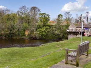 a bench sitting on the grass next to a river at River View Cottage in Knaresborough