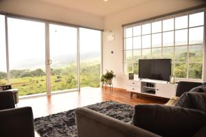 uma sala de estar com televisão e janelas grandes em Thumpers Cottage em Kalawana