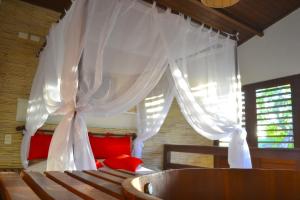 um quarto com uma cama com cortinas brancas e almofadas vermelhas em Naquela Jericoacoara em Jericoacoara