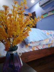 um vaso roxo com flores amarelas numa mesa ao lado de uma cama em Vivacity Megamall Jazz Suite 3BR 7pax #Joyoustayz em Kuching