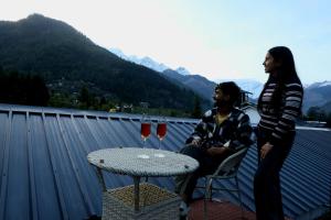 Hotel Old Manali - The Best Riverside Boutique Stay with Balcony and Mountain Views في مانالي: رجل وامرأة يجلسان في شرفة ذات كؤوس للنبيذ