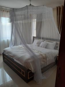 una camera con letto a baldacchino con lenzuola e cuscini bianchi di VILLA FIORI APARTMENTS a Arua
