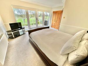 - une chambre avec un grand lit et une télévision dans l'établissement Golf Course View - Large Four Bed Home with Garden and Parking - New Forest and Beach Links, à Ferndown
