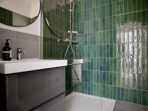 La salle de bains est pourvue de carrelage vert, d'un lavabo et d'une douche. dans l'établissement Apartmenthaus Hamburg Les Jardins, à Hambourg