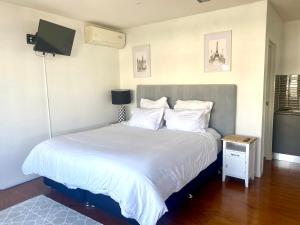 um quarto com uma cama com lençóis brancos e uma televisão em Self contained guest house - sleeps 4 em Gold Coast