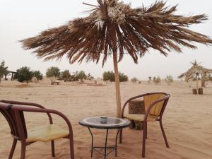 two chairs and a table under an umbrella in the desert at Volunteer in desert in Mhamid