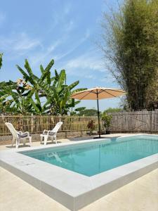 einen Pool mit 2 Stühlen und einem Sonnenschirm in der Unterkunft Lanna House Lanna Hut Chiangmai in Chiang Mai