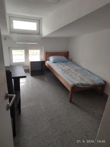 a bedroom with a bed and a desk and two windows at Apartman in Vogošća