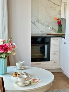 a white kitchen with a table with two cups and roses at Apartament Grottgera in Gdynia
