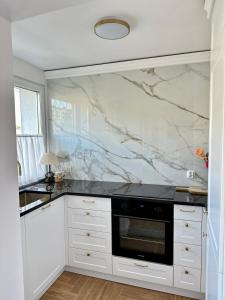 a kitchen with white cabinets and a marble wall at Apartament Grottgera in Gdynia