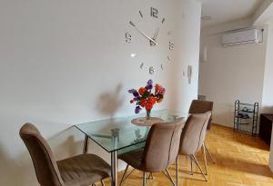 een eetkamer met een glazen tafel met stoelen en een klok bij Apartman Panorama in Požarevac