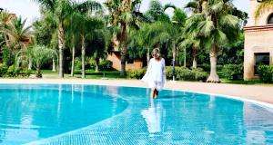 a woman in a white dress walking into a swimming pool at La Perle de l'Atlas by Golf Resort in Marrakech