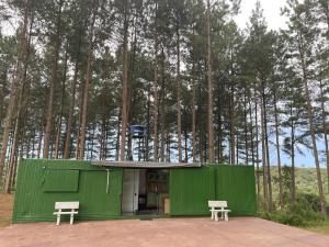 a green building with two benches in front of trees at Chácara no bosque in São Bento do Sul