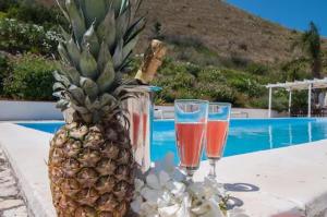 een ananas en twee glazen op een tafel naast een zwembad bij villa costanza in Cefalù