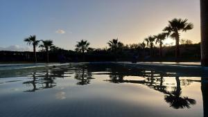 - une piscine avec des palmiers et le coucher du soleil dans l'établissement Dar De Santis, à Azemmour