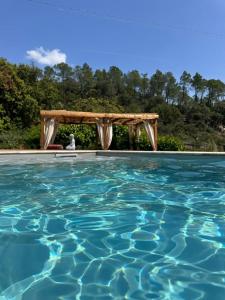 uma piscina com uma pérgula de madeira e água azul em Idyllic Roulotte em Les Assions