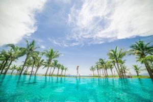 a person standing in the water in front of palm trees at Aqua Vista Hoi An Beachfront Villas in Hoi An