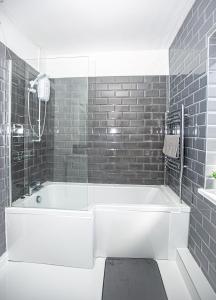 a white bath tub in a bathroom with black tiles at Libra House retreat, Caswell Bay in Swansea