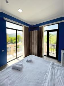 a bedroom with a large bed with blue walls and large windows at Khidikari Hotel in Ambrolauri