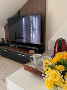 a living room with a tv and flowers on a table at Sobrado Charmoso e Aconchegante / Santa Felicidade PR in Curitiba