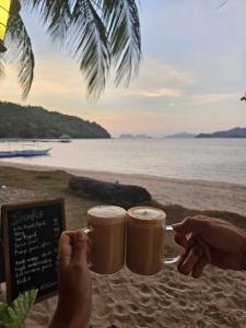 dos personas sosteniendo tazas de café en una mesa en la playa en DK2 Resort - Hidden Natural Beach Spot - Direct Tours & Fast Internet en El Nido