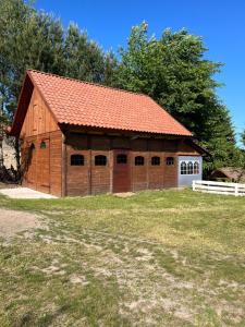 a brown barn with an orange roof on a field at Łęgowska Dolina in Olecko