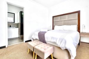 a white bedroom with a large bed and a stool at Sandton Lux, CBD, 2 Bedroom & 2 Ensuite, No Load shedding in Johannesburg