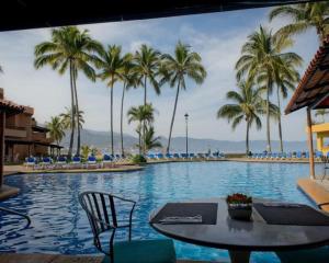 a swimming pool with a table and chairs and palm trees at Los Tules Ocean Front Studio 901 - 2nd floor in Puerto Vallarta