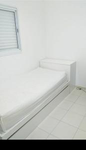 uma cama branca num quarto branco com uma janela em Nosso canto em Guaratinguetá