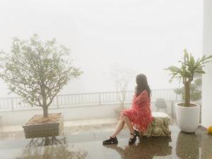 White House - Nhà khách Báo nhân dân TAM ĐẢO في Vĩnh Phúc: امرأة ترتدي ثوب احمر تجلس على كرسي تحت المطر