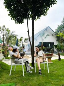 Đông Sơn Mountain Villa في Bắc Ninh: اثنتان من النساء يجلسن في كراسي الحديقة يتحدثن على الهواتف الخلوية