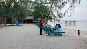 a group of people sitting on benches on the beach at Madu Tiga Beach and Resort in Tanjung Pinang