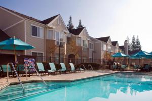 a swimming pool with chairs and umbrellas next to houses at Residence Inn Pleasant Hill Concord in Pleasant Hill