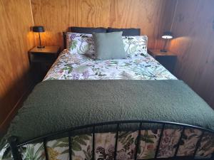 1 cama en un dormitorio con 2 lámparas en las mesas en Crinkly Cottage en Te Kuiti