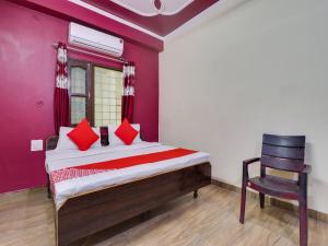 a bedroom with a bed with red pillows and a chair at OYO Hotel Kesariya Bhawan Home Stay in Dehradun