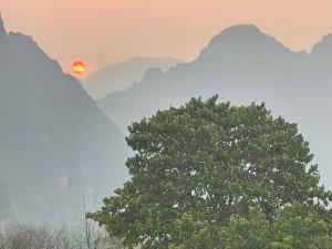 a tree in front of mountains with the sun setting at Blue Sunset Hostel in Vang Vieng
