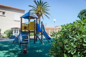 un parco giochi con scivolo in un cortile con una palma di Hotel L'ondine a Algajola