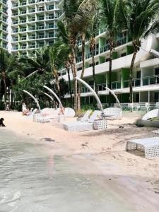 a beach with white chairs and palm trees and a building at Azure Urban Residences Beach and Resort by Vookley in Manila