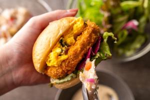 una mano sosteniendo un sándwich de pollo con un tenedor en Hotel Mystays Premier Hamamatsucho, en Tokio